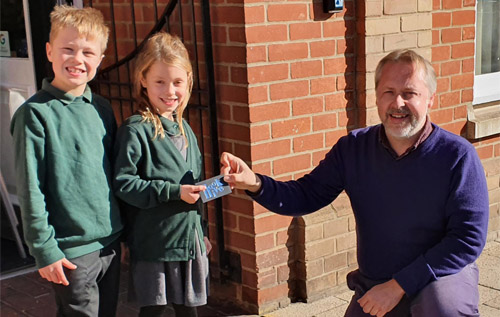 Ben Miller of The Book Hive, Aylsham, presents the prize token to Eve Hedges, with her brother Rowan, outside Aylsham Library.
