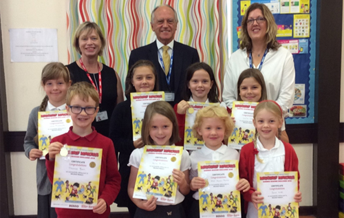 Cllr Greg Peck (back row, centre) with Reepham Primary School head Catherine Ogle (left), Aylsham and Reepham Libraries manager Sara Caistor (right), and Reepham Primary School pupils who were presented with Super Achiever medals and certificates.